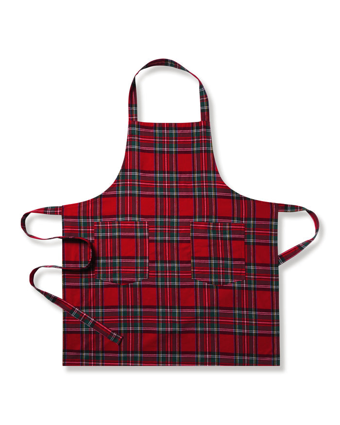 Two Petite Plume Adult Aprons in Imperial Tartan hang on a wooden rack with a patterned white dish towel. Perfect for holiday baking, a wooden spoon and spatula peek from an apron pocket against a warm, beige wall backdrop, creating an inviting scene for cozy cooking adventures.