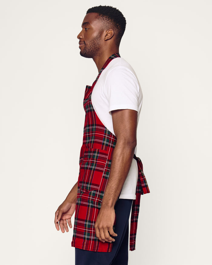 Two Petite Plume Adult Aprons in Imperial Tartan hang on a wooden rack with a patterned white dish towel. Perfect for holiday baking, a wooden spoon and spatula peek from an apron pocket against a warm, beige wall backdrop, creating an inviting scene for cozy cooking adventures.