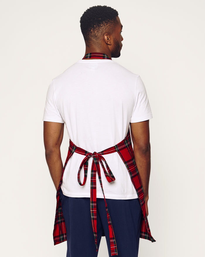 Two Petite Plume Adult Aprons in Imperial Tartan hang on a wooden rack with a patterned white dish towel. Perfect for holiday baking, a wooden spoon and spatula peek from an apron pocket against a warm, beige wall backdrop, creating an inviting scene for cozy cooking adventures.
