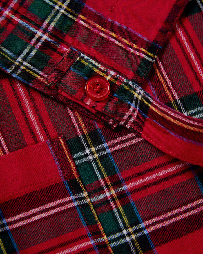 Two Petite Plume Adult Aprons in Imperial Tartan hang on a wooden rack with a patterned white dish towel. Perfect for holiday baking, a wooden spoon and spatula peek from an apron pocket against a warm, beige wall backdrop, creating an inviting scene for cozy cooking adventures.