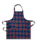 Two Adult Aprons in Windsor Tartan by Petite Plume, ideal for holiday baking, hang on a wooden rack beside a striped towel. One apron is labeled Dad, with a wooden spoon in its pocket. The background features a cozy warm beige wall.