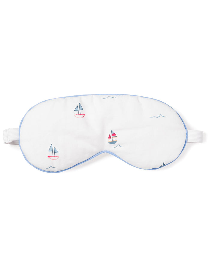 The Adults Twill Sleep Mask in Bateau by Petite Plume is a white mask with light blue trim and colorful sailboat designs. It has an adjustable strap for a luxurious sleep experience and makes a perfect monogrammed gift for those who appreciate elegance at bedtime.