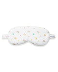 A woman with wavy blonde hair wears the Adult's Twill Sleep Mask in Good Luck Charms and matching patterned pajamas, gazing to the side against a plain neutral background.