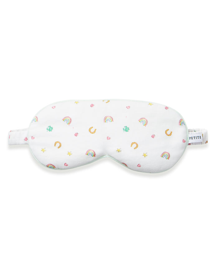 A woman with wavy blonde hair wears the Adult's Twill Sleep Mask in Good Luck Charms and matching patterned pajamas, gazing to the side against a plain neutral background.