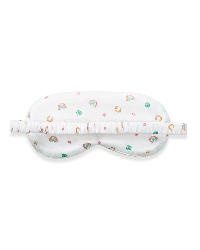 A woman with wavy blonde hair wears the Adult's Twill Sleep Mask in Good Luck Charms and matching patterned pajamas, gazing to the side against a plain neutral background.