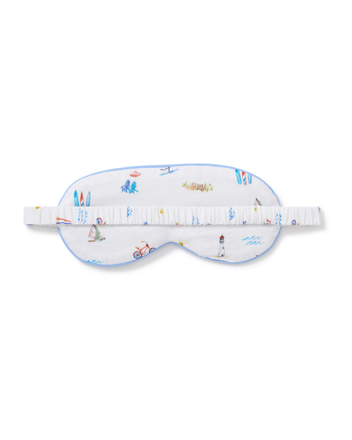 An Adult’s Twill Sleep Mask in Summer Nostalgia, featuring colorful beach-themed illustrations—surfboards, a lighthouse, waves, and a bike—on a white background with a matching elastic strap.