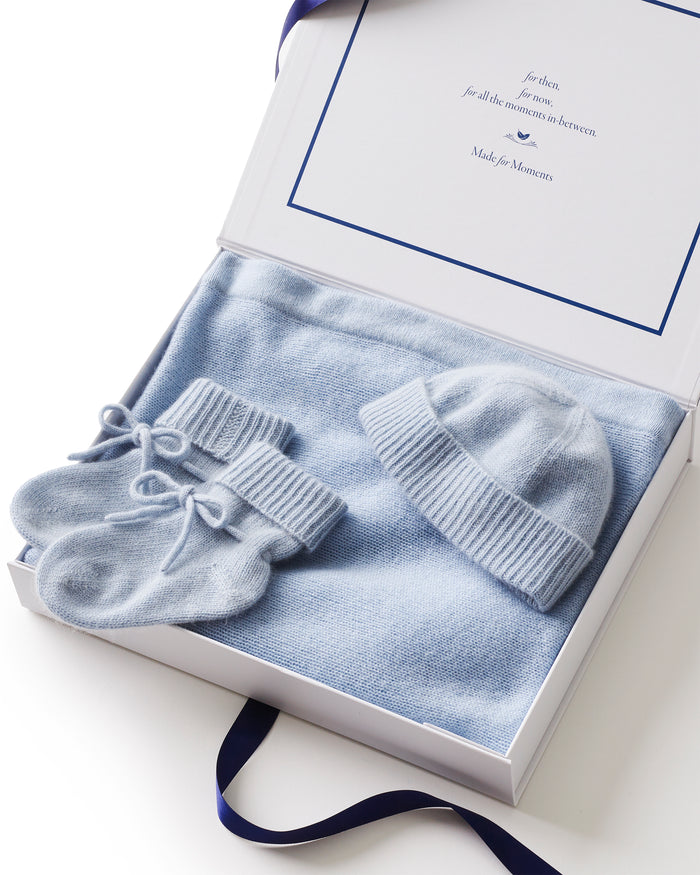 The Baby Cashmere Bundle in Light Blue features a neatly folded knit blanket, a matching baby hat, and knit booties with ribbons, all beautifully arranged on a white background.