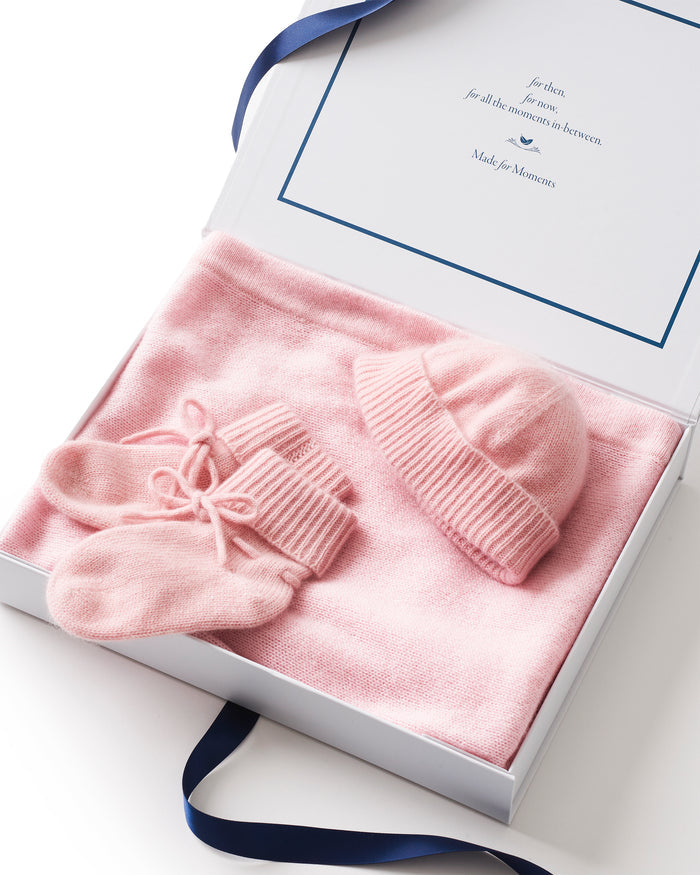 The Baby Cashmere Bundle in Rose features a neatly folded pink baby blanket, matching knit booties, and a ribbed knit hat, all displayed on a white background.