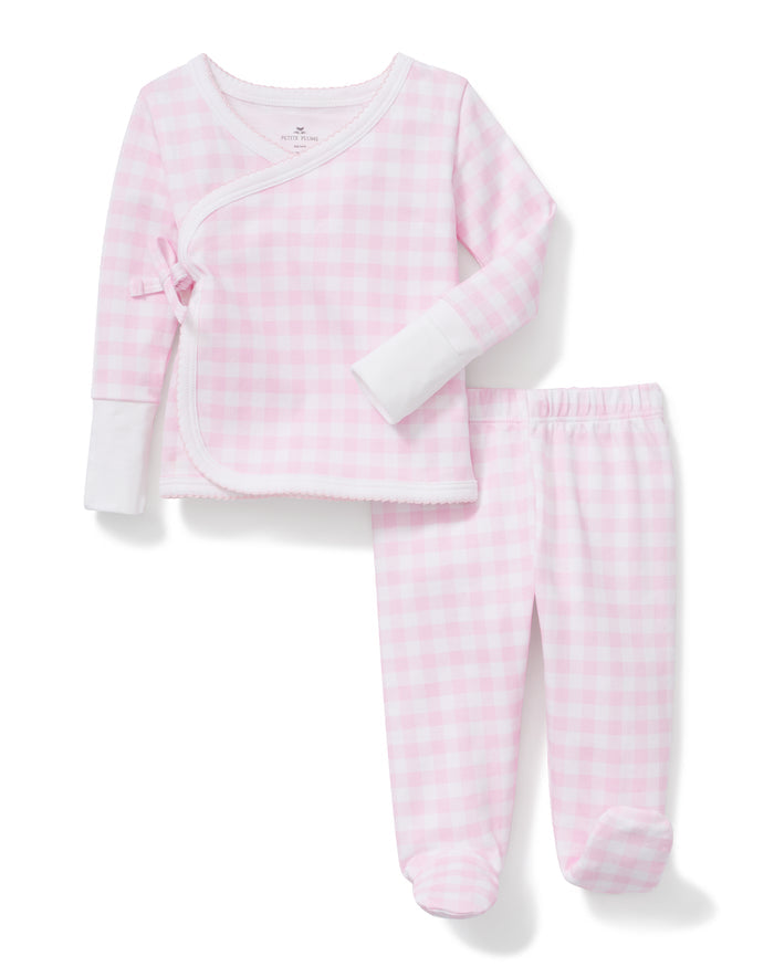The Baby Pima Wrap Set in Pink Gingham features a pink and white checkered long-sleeve pajama top with a front side tie, white cuffs, and matching footed pants.