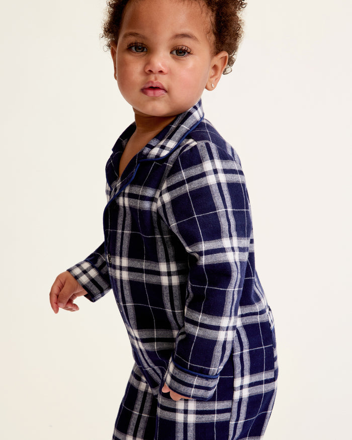 The Baby's Brushed Twill Classic Romper in Oxford Tartan is a full-length, long-sleeve children's onesie featuring a navy, white, and gray plaid pattern with a button-up front, collar, and snap leg closures.