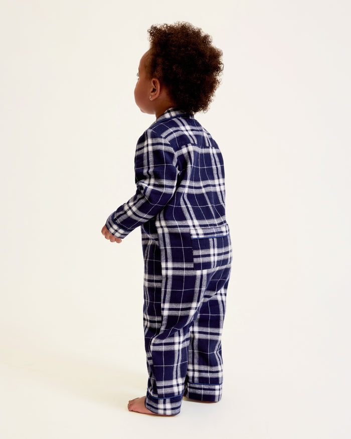 The Baby's Brushed Twill Classic Romper in Oxford Tartan is a full-length, long-sleeve children's onesie featuring a navy, white, and gray plaid pattern with a button-up front, collar, and snap leg closures.