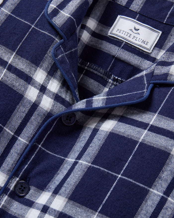 The Baby's Brushed Twill Classic Romper in Oxford Tartan is a full-length, long-sleeve children's onesie featuring a navy, white, and gray plaid pattern with a button-up front, collar, and snap leg closures.