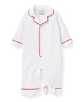 A toddler in Petite Plumes Babys Twill Romper in White with Red Piping stands against a plain background, looking up curiously with slightly tousled hair, as if just woken from sleepwear comfort.
