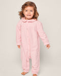 A young child with wavy brown hair is wearing Petite Plumes Babys Flannel Madeline Romper in Pink, featuring a Peter Pan collar and made of chemical-free flame-retardant material. They stand barefoot against a plain background.