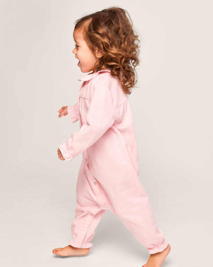A curly-haired toddler joyfully walks in Petite Plumes Babys Flannel Madeline Romper in Pink, a brushed cotton onesie with front buttons. Theyre barefoot against a plain, neutral background.