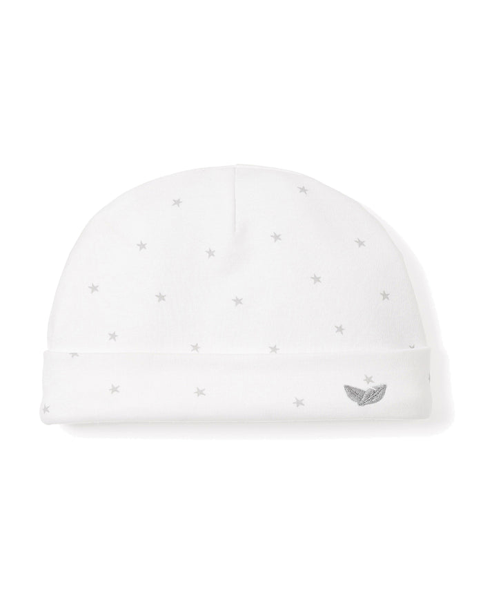A white baby hat from Petite Plume features soft Peruvian Pima cotton with gray star patterns. It has a folded brim and a small embroidered gray logo of two leaves, representing premium soft baby clothing.