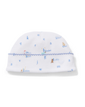 Introducing the Baby’s Pima Hat in Letters and Lullabies—a white baby hat featuring a blue zigzag trim, playful animal illustrations, stars, teddy bears, scattered blue letters, whimsical motifs, and sweet words like “blanket.”.