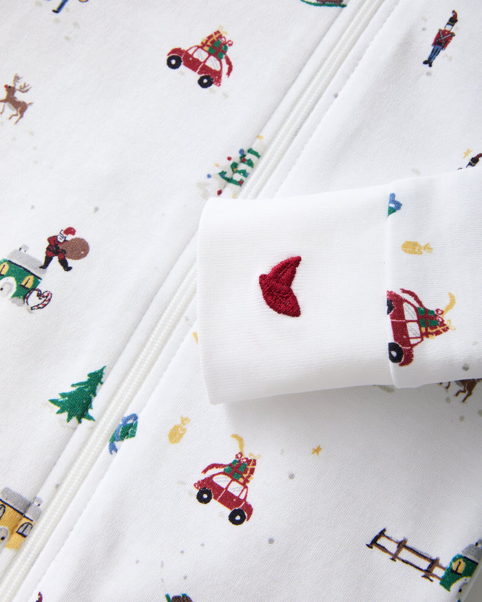 The Baby's Pima Romper in Holiday Town is a white footed sleeper with a diagonal zipper, featuring colorful prints of Christmas trees, reindeer, cars, snowmen, fences, and hearts.