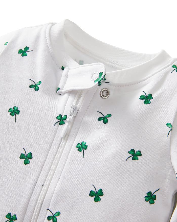 The Baby's Pima Romper in Shamrocks is a white footed onesie with long sleeves, featuring a pattern of small green clovers and a front zipper from neckline to leg.