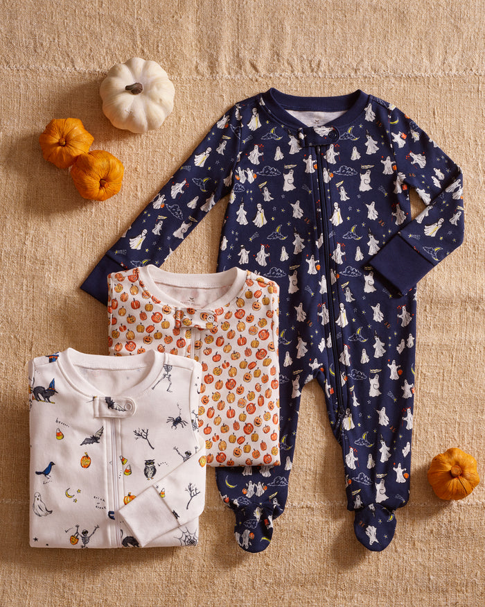 The Baby's Pima Romper in Spooky Slumber is a navy blue, long-sleeve, footed sleeper with a front zipper and features white polar bears in scarves and hats, stars, and geometric shapes on soft fabric.