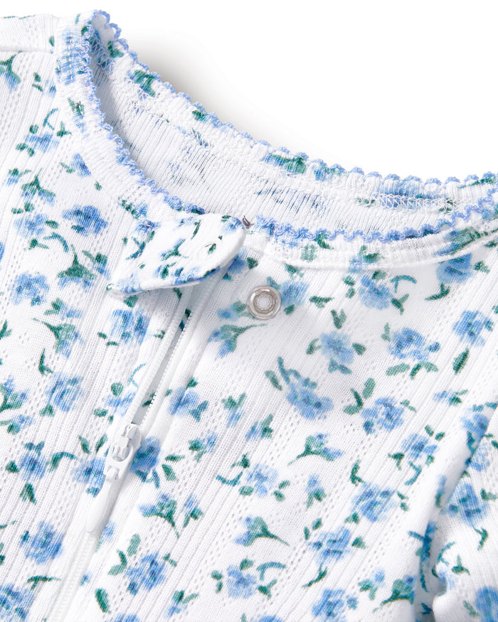 The Baby's Pointelle Footie Romper in Blue Floral is a white footed onesie with a front zipper, decorated with small blue flowers and green leaves.