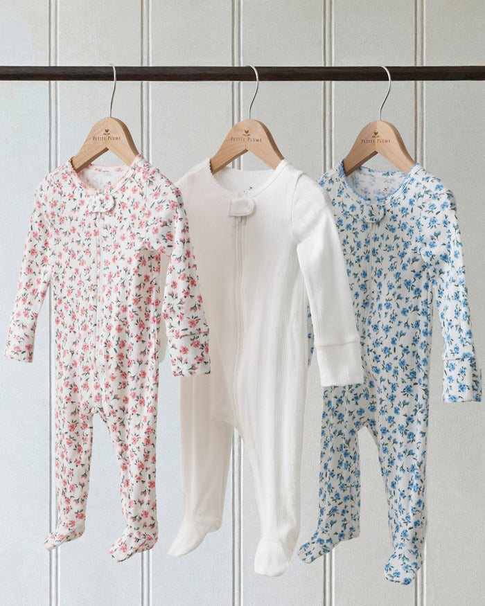 The Baby's Pointelle Footie Romper in Blue Floral is a white footed onesie with a front zipper, decorated with small blue flowers and green leaves.