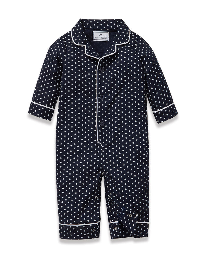 The Baby's Twill Classic Romper in Midnight Hearts is a navy blue onesie with long sleeves and legs, featuring a white heart pattern and white piping on the collar, cuffs, and front.