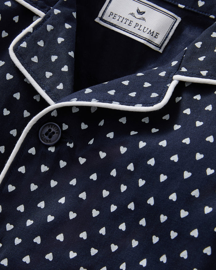 The Baby's Twill Classic Romper in Midnight Hearts is a navy blue onesie with long sleeves and legs, featuring a white heart pattern and white piping on the collar, cuffs, and front.
