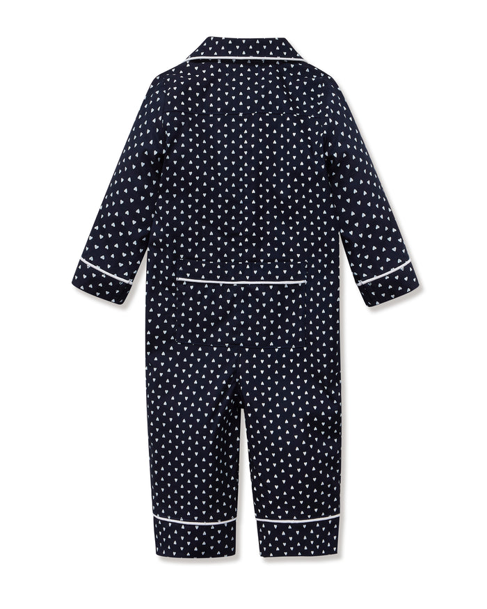 The Baby's Twill Classic Romper in Midnight Hearts is a navy blue onesie with long sleeves and legs, featuring a white heart pattern and white piping on the collar, cuffs, and front.