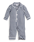 A blonde toddler sits wearing Petite Plumes Babys Twill Winter Romper in Navy Gingham. One arm is raised, and the child looks down with a slight smile. Wooden blocks are scattered in front of them.