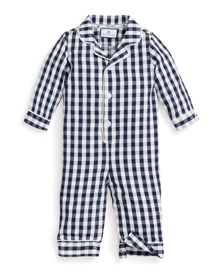 A blonde toddler sits wearing Petite Plumes Babys Twill Winter Romper in Navy Gingham. One arm is raised, and the child looks down with a slight smile. Wooden blocks are scattered in front of them.