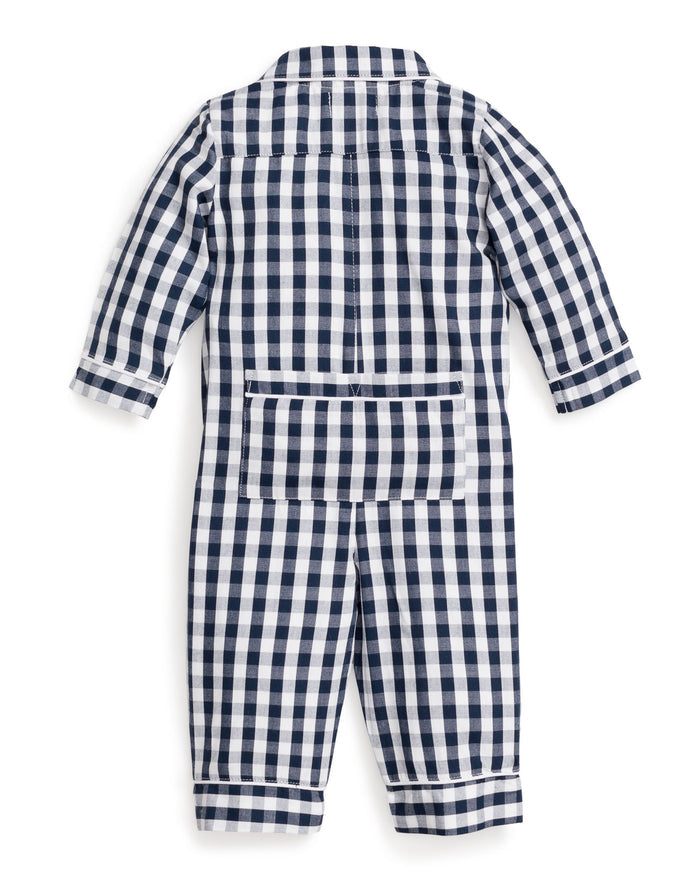 A blonde toddler sits wearing Petite Plumes Babys Twill Winter Romper in Navy Gingham. One arm is raised, and the child looks down with a slight smile. Wooden blocks are scattered in front of them.