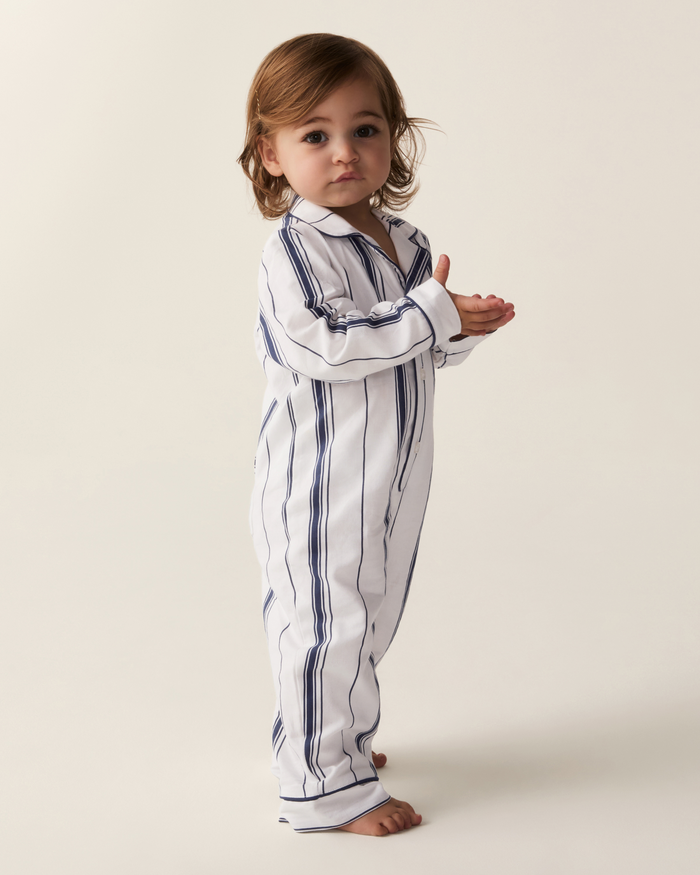 A toddler with light brown hair stands barefoot, clapping their hands and gazing slightly to the side while wearing the Baby’s Twill Classic Romper in Parlor Stripe against a plain background.