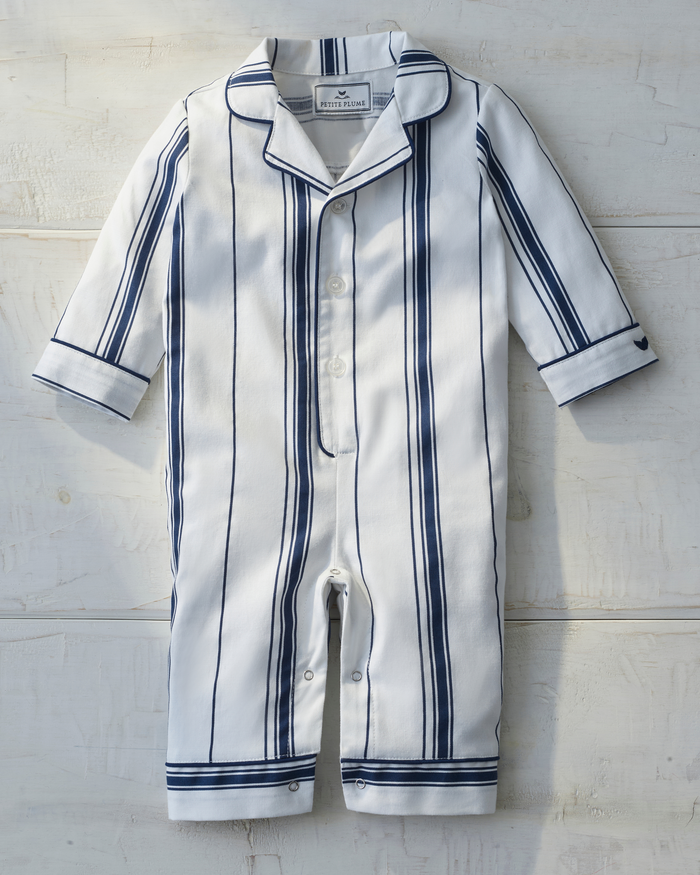 The Baby’s Twill Classic Romper in Parlor Stripe is displayed against a light wooden background, featuring navy blue vertical stripes on white fabric, a collar, long sleeves, and buttons down the front.