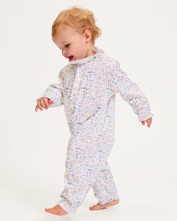 The Baby's Twill Madeline Romper in Baking Spirits Bright features long sleeves, a ruffled collar and cuffs, pastel kitchen print on white, front buttons, and snap closures at the legs for easy dressing.