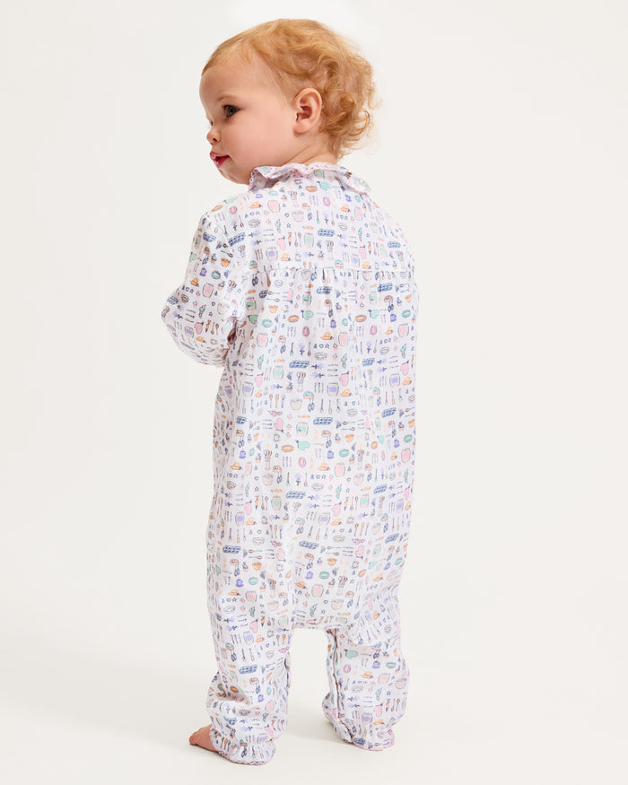 The Baby's Twill Madeline Romper in Baking Spirits Bright features long sleeves, a ruffled collar and cuffs, pastel kitchen print on white, front buttons, and snap closures at the legs for easy dressing.