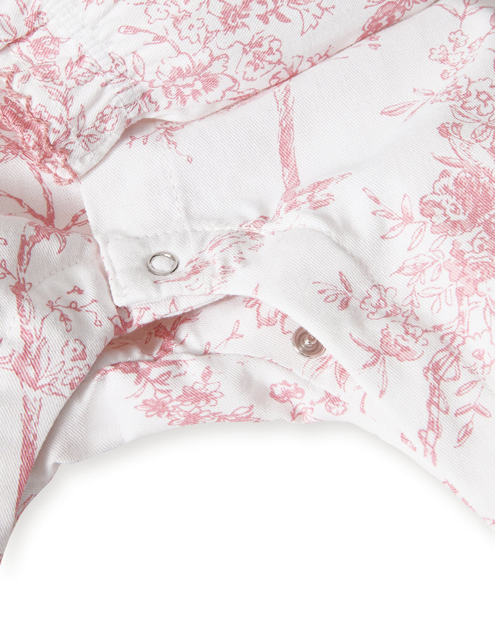 The Baby's Twill Madeline Romper in Pink Timeless Toile features long sleeves, pink toile floral and tree patterns, ruffled cuffs and collar, and convenient inseam snaps for easy diaper changes.