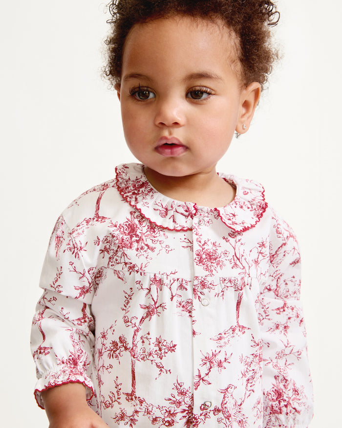 The Baby's Twill Madeline Romper in Red Timeless Toile features long sleeves, a ruffled collar, red floral print, and snap buttons down the front and legs.
