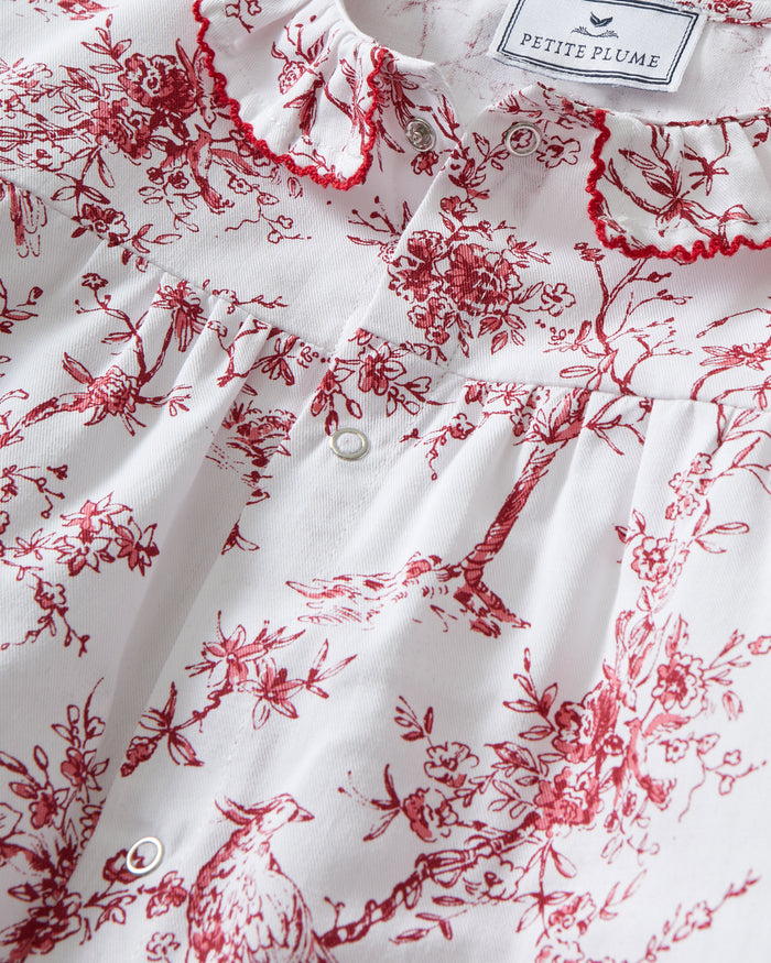 The Baby's Twill Madeline Romper in Red Timeless Toile features long sleeves, a ruffled collar, red floral print, and snap buttons down the front and legs.