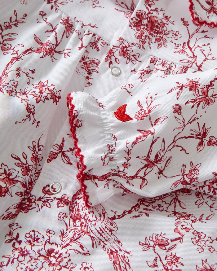 The Baby's Twill Madeline Romper in Red Timeless Toile features long sleeves, a ruffled collar, red floral print, and snap buttons down the front and legs.
