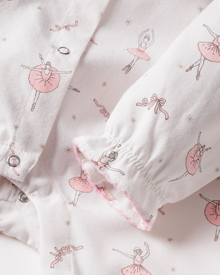 Close-up of Petite Plumes Babys Flannel Madeline Romper in Sugar Plum Fairy, showcasing white fabric adorned with pink ballet dancers and ribbons. The romper features buttoned detailing, gathered sleeves with pink trim, and is made from flame-retardant material for safe and charming childrens sleepwear.