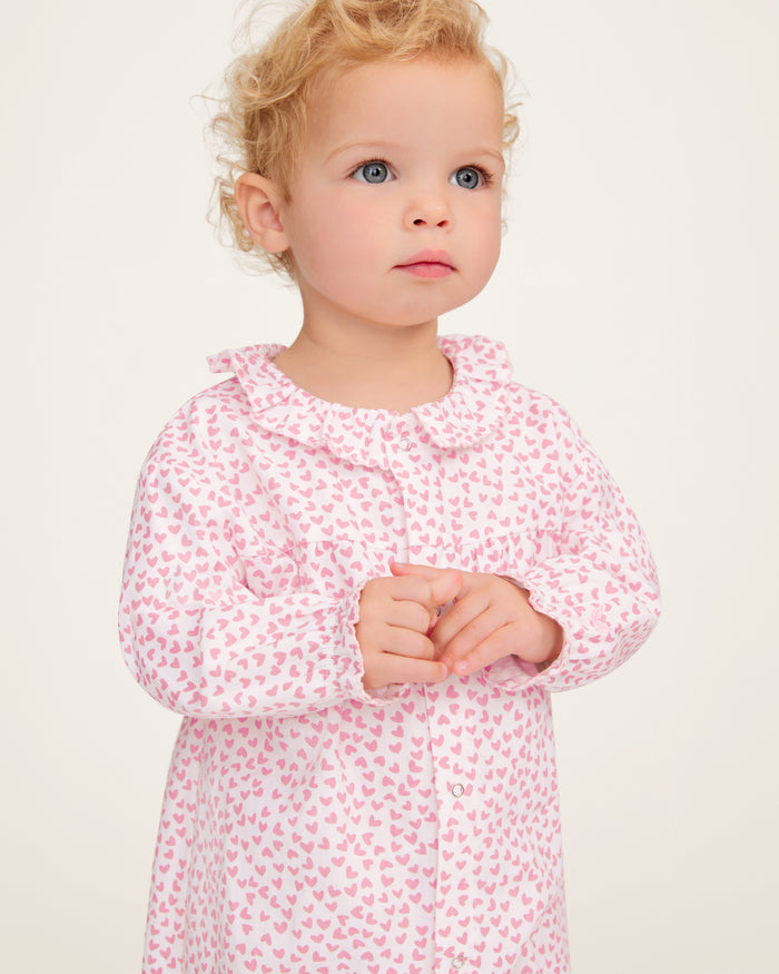 The Baby's Twill Madeline Romper in Sweethearts is a pink and white long-sleeve romper featuring a ruffled collar and cuffs, adorned with a small pink heart pattern.