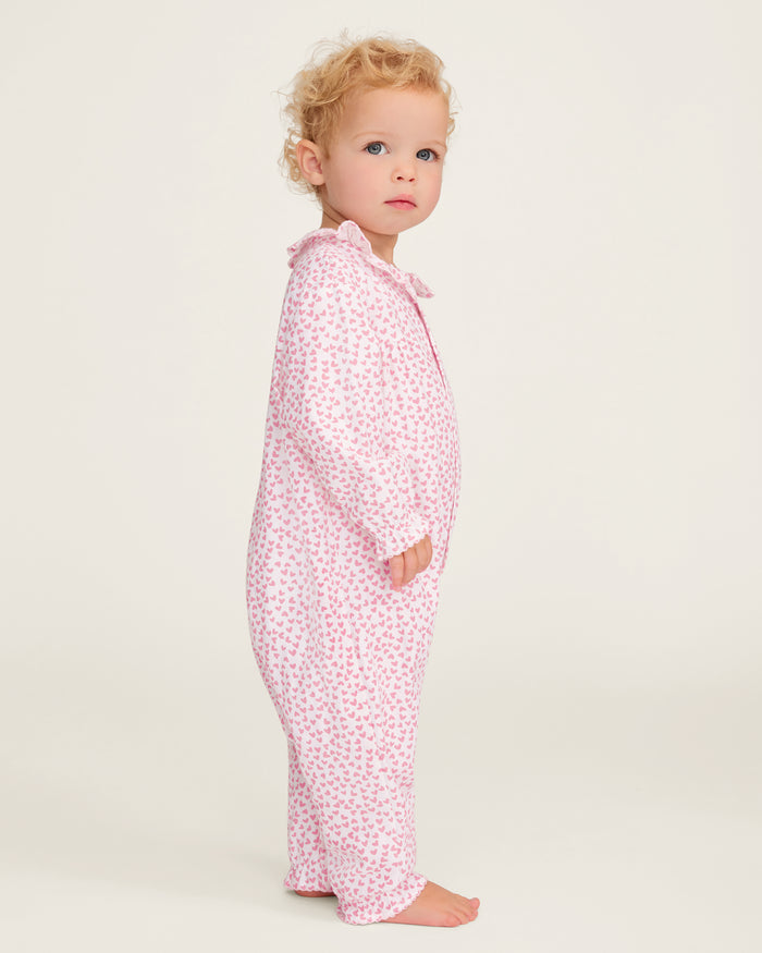 The Baby's Twill Madeline Romper in Sweethearts is a pink and white long-sleeve romper featuring a ruffled collar and cuffs, adorned with a small pink heart pattern.