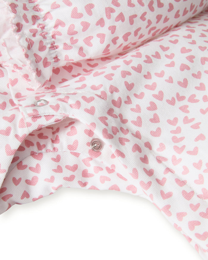 The Baby's Twill Madeline Romper in Sweethearts is a pink and white long-sleeve romper featuring a ruffled collar and cuffs, adorned with a small pink heart pattern.