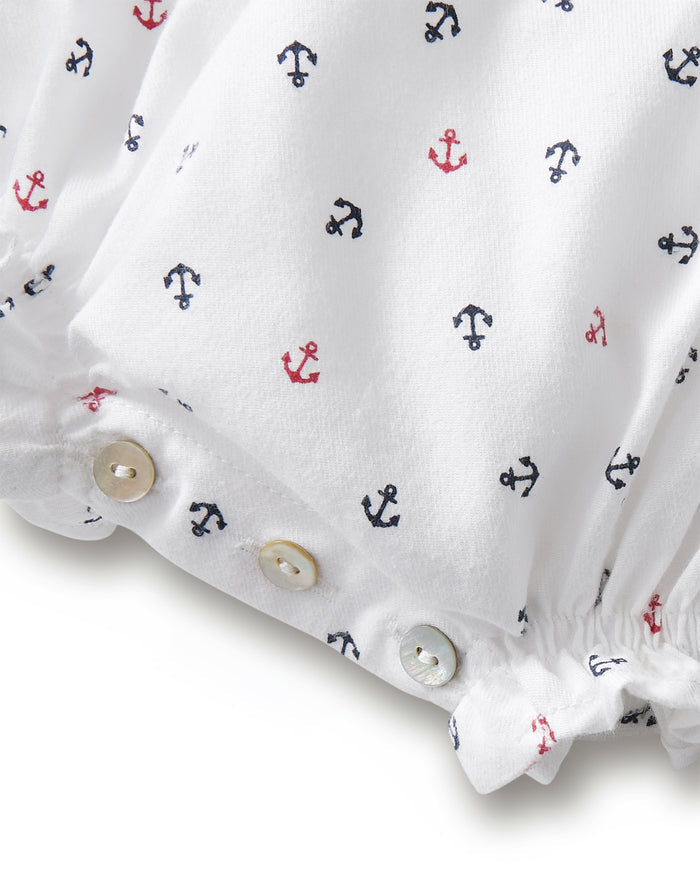 Crafted from white twill fabric adorned with red and navy blue anchor motifs, the Baby’s Twill Ruffled Romper in Anchors Away White features three white buttons along the bottom hem and gathered edges, making it a charming choice for babies or toddlers.