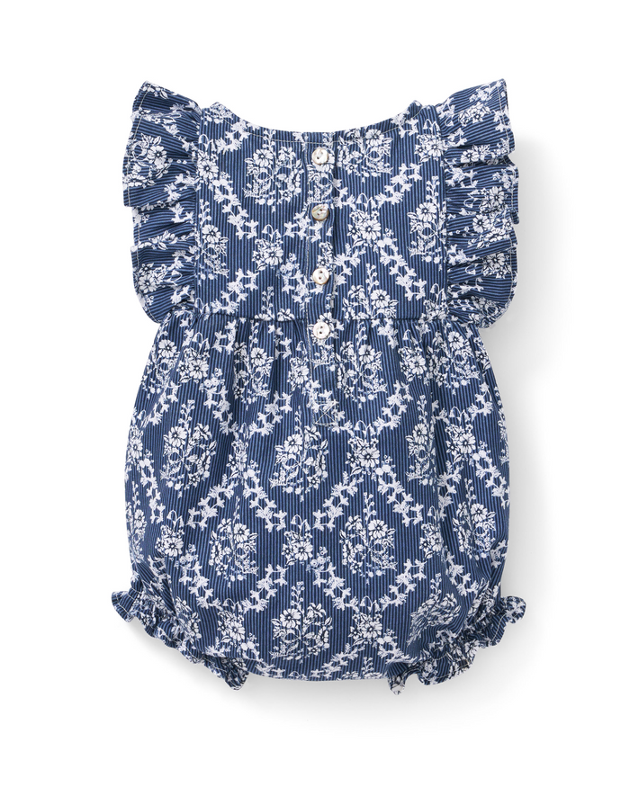 The Baby’s Twill Ruffled Romper in Innkeeper Trellis features a blue and white striped background with a delicate floral pattern, ruffled sleeves, white buttons down the front, and elastic leg openings.