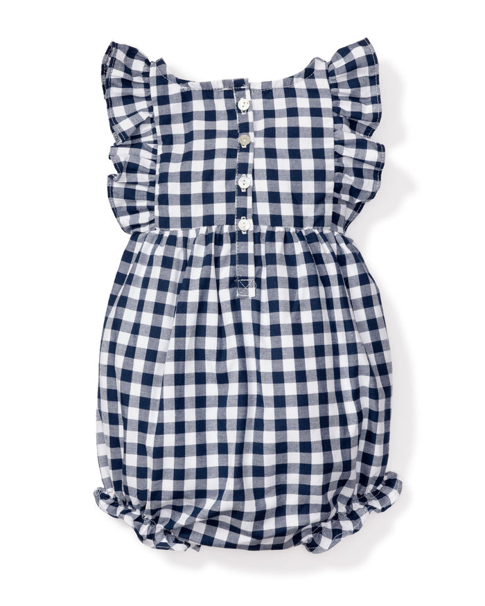 The Petite Plume Babys Twill Ruffled Romper in Navy Gingham combines style and safety with its flame-retardant fabric, ruffled sleeves, button-up front with white buttons, and elasticized leg openings, all in an elegant navy blue and white checkered design.