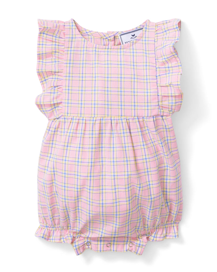 A toddler with curly hair wears the Baby's Twill Ruffled Romper in Peony Plaid, featuring ruffled sleeves, standing barefoot against a plain light background and looking slightly to the side.
