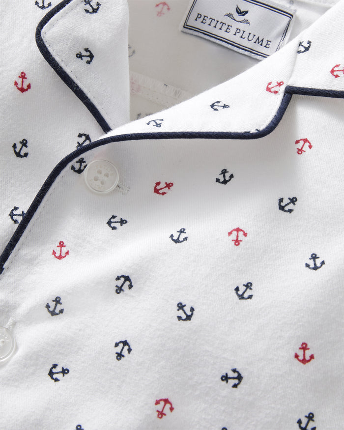 Close-up of the Baby’s Twill Summer Romper in Anchors Away White, featuring a white fabric with small red and blue anchor patterns, navy piping along the collar, white buttons, and a PETITE PLUME label inside the neckline.