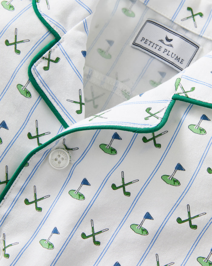The Baby's Twill Summer Romper in Fairway Stripe is a short-sleeved, button-down romper with green piping, decorated with golf clubs and holes on white fabric with blue vertical stripes.